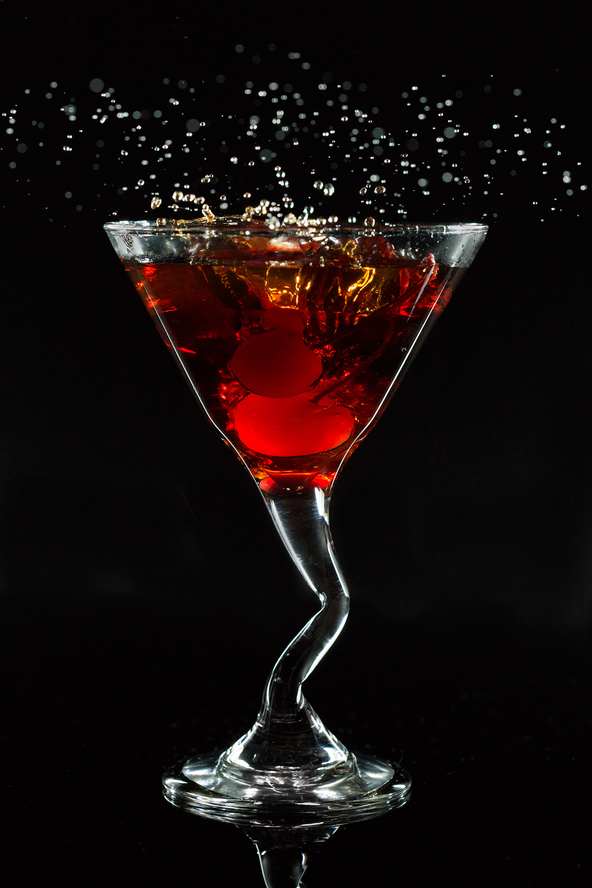 manhattan drink with cherries falling into it and spraying liquid above the glass